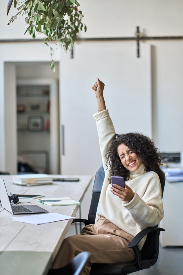Happy woman on her phone with an arm in the air in triumph